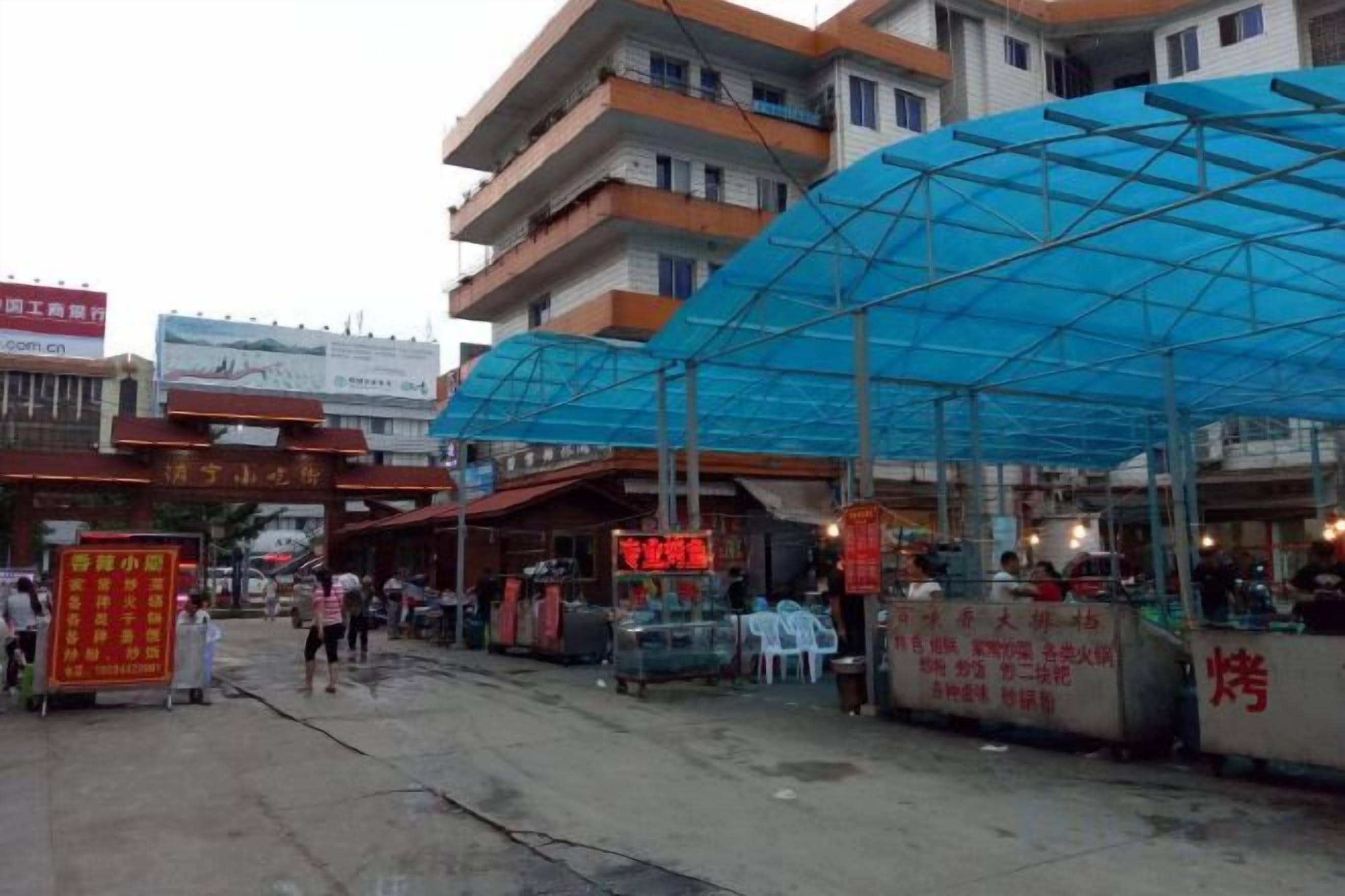 A street with a blue canopy structure, a red signboard, and a building with multiple floors.