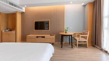 Een moderne hotelkamer met een groot bed, een aan de muur bevestigde televisie, een tafeltje met stoelen en een bureau met een stoel.