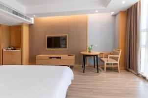 Una habitación de hotel moderna con una cama grande, un televisor montado en la pared, una pequeña mesa con sillas y un escritorio con una silla.