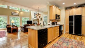 A spacious kitchen with wooden cabinets, a dishwasher, a microwave, and a refrigerator. There is a dining area with a table and chairs, and a living room with a sofa and a TV. - Fairway to Seven - King Bed, Big-screen TVs & Golf Course Views (Jasper)