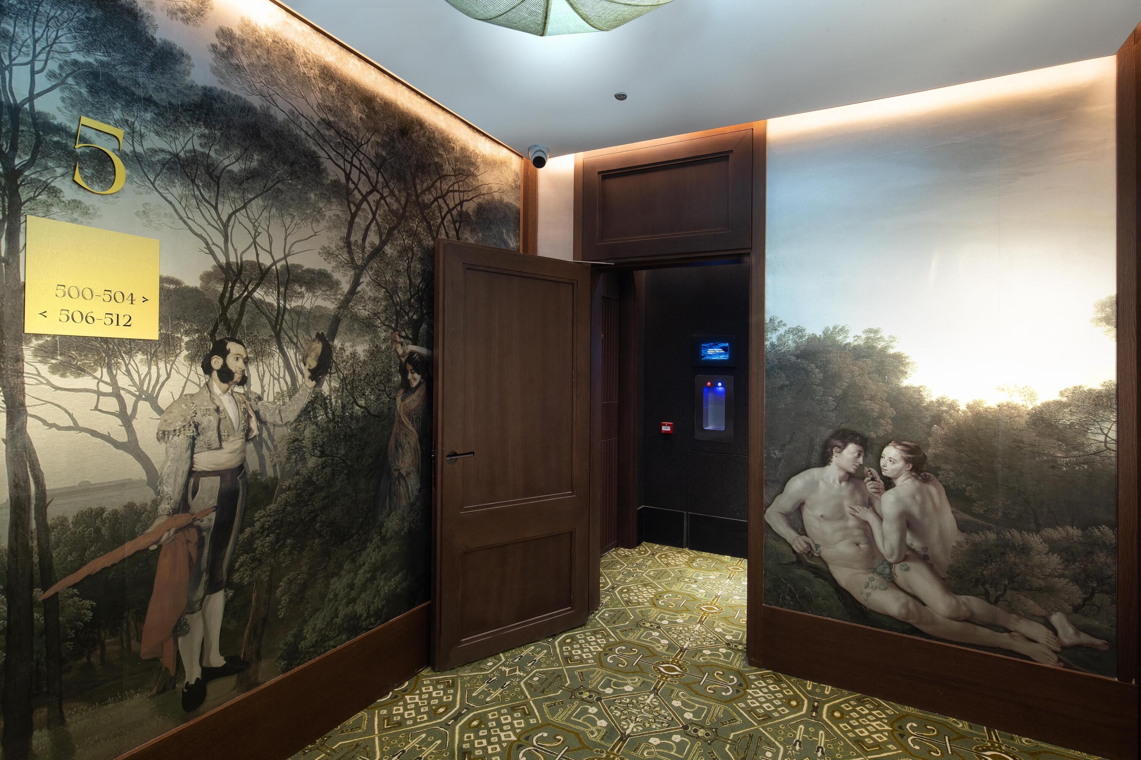 Un pasillo con un mural, una puerta y una pantalla digital.