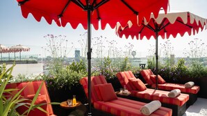 A rooftop lounge with red-striped sofas, red umbrellas, and a city view. - Hotel Montera Madrid, Curio Collection By Hilton (Madrid)