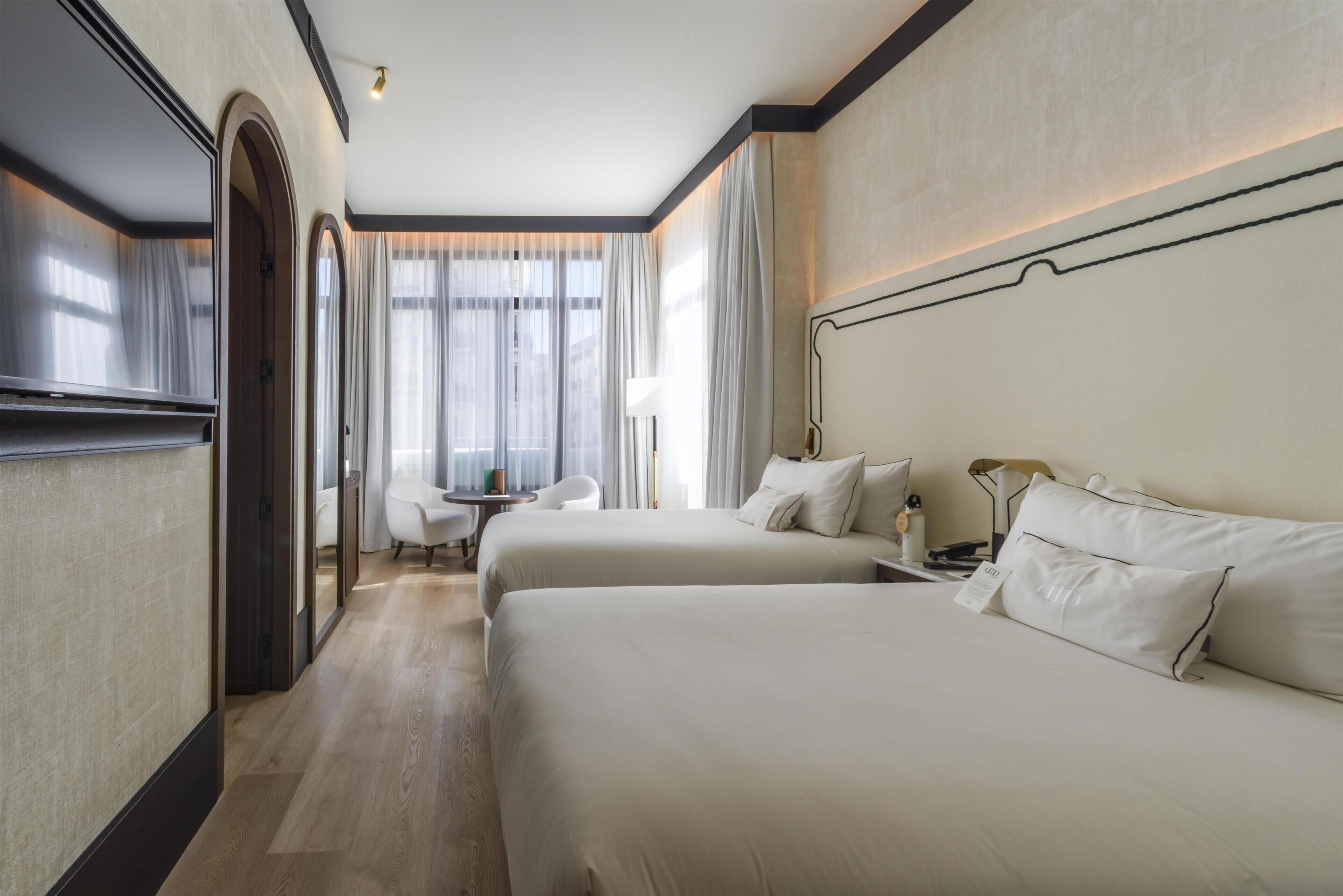 Hotellihuone, jossa on kaksi sänkyä, työpöytä, tuoli ja lamppu.