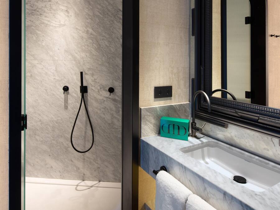 Un baño moderno con ducha envuelta en vidrio, encimera de mármol, lavamanos y un espejo grande.
