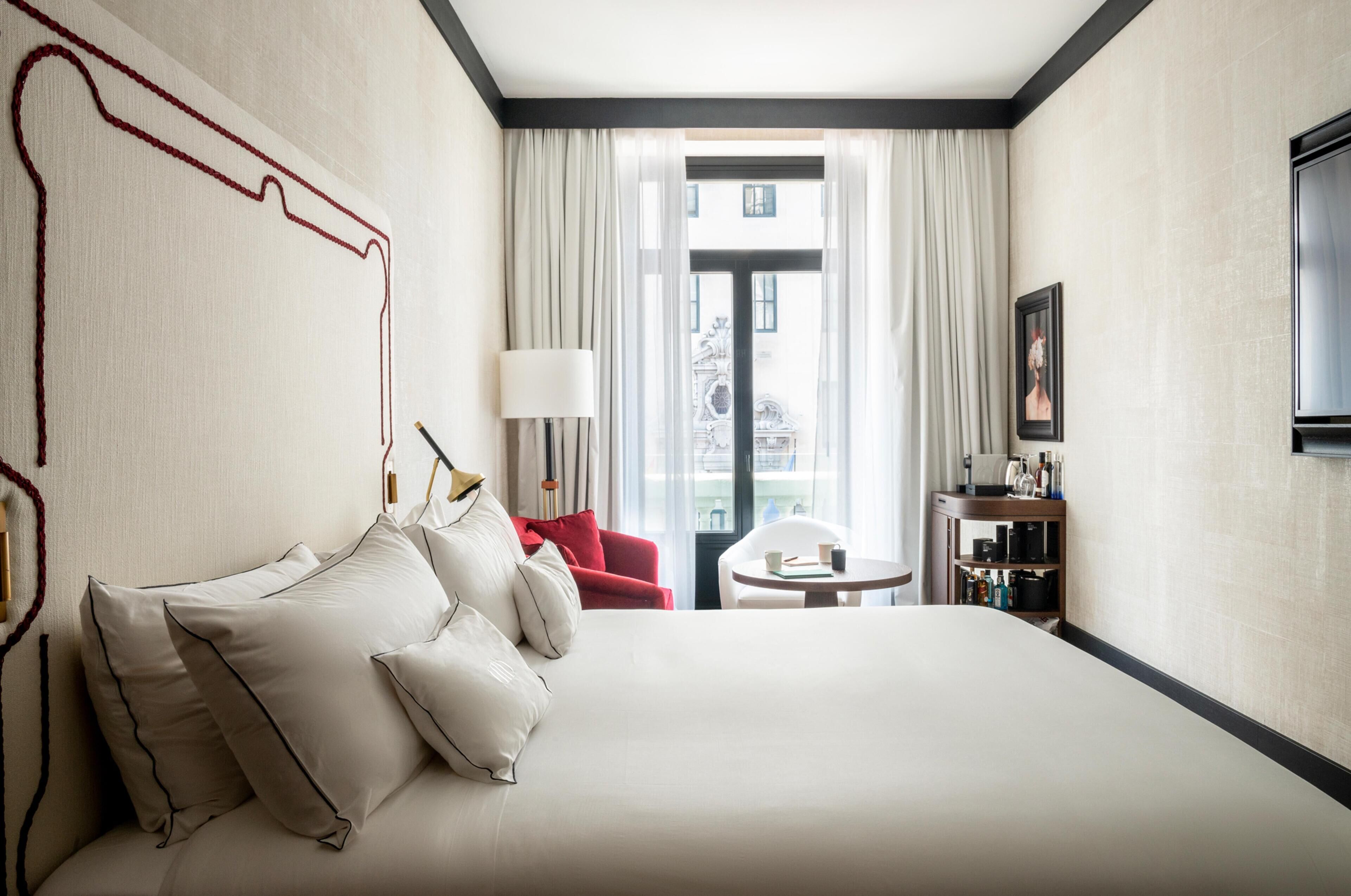 Una habitación de hotel con una cama grande, una silla roja, una mesita redonda y un televisor en la pared.