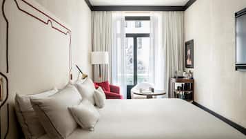 Una habitación de hotel con una cama grande, una silla roja, una mesita redonda y un televisor en la pared.
