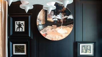 A room with a black wall, a round mirror, framed pictures, a white armchair, and a patterned rug.
