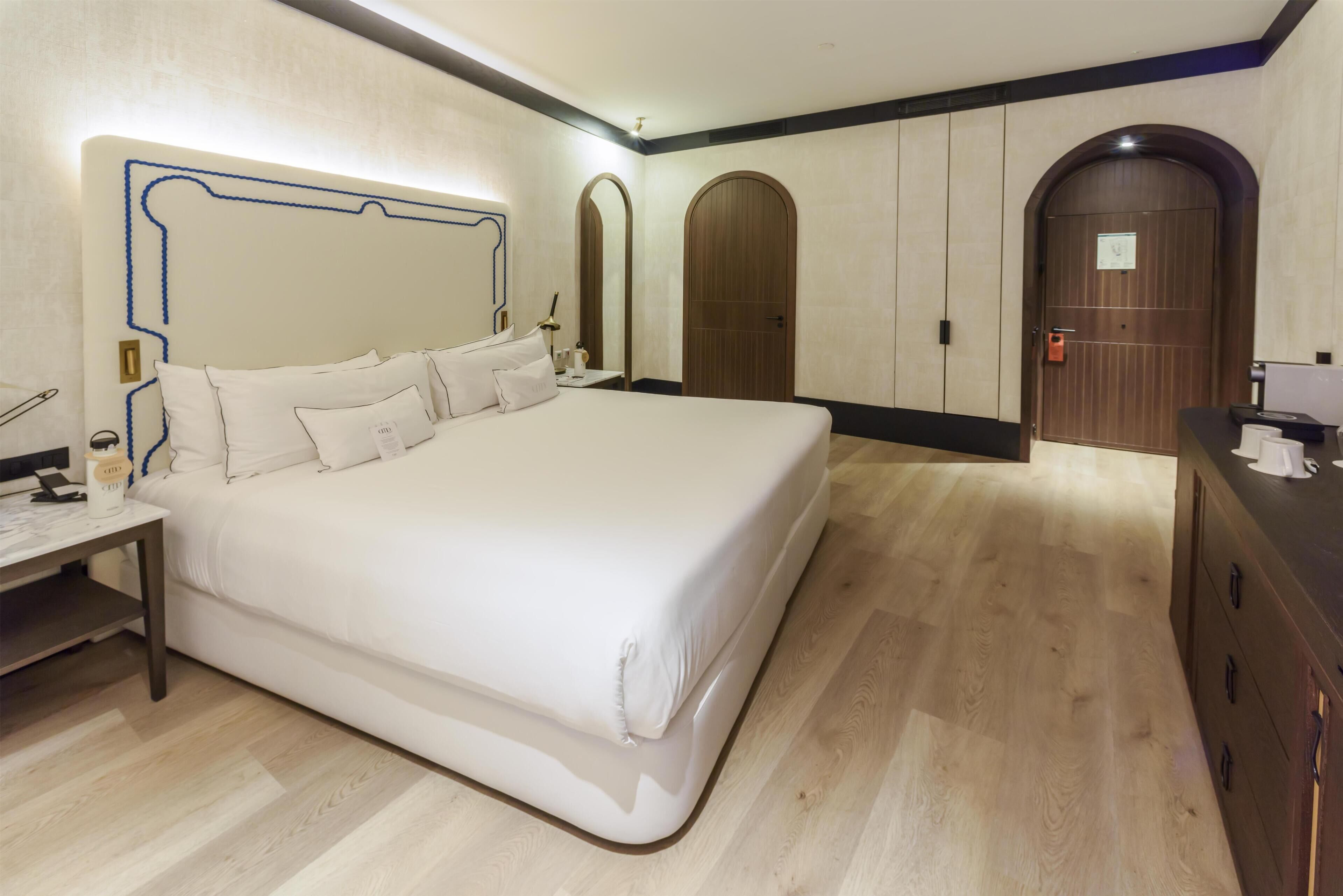 A hotel room with a large bed, a bedside table, a desk, and a wardrobe.