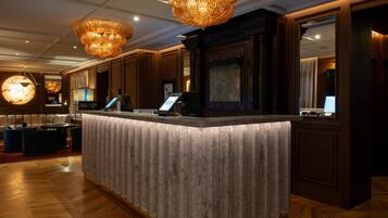 A hotel reception area with a marble counter, wooden paneling, and large chandeliers.