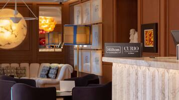 A hotel lobby with a marble reception desk, a large chandelier, a sofa, and a statue.