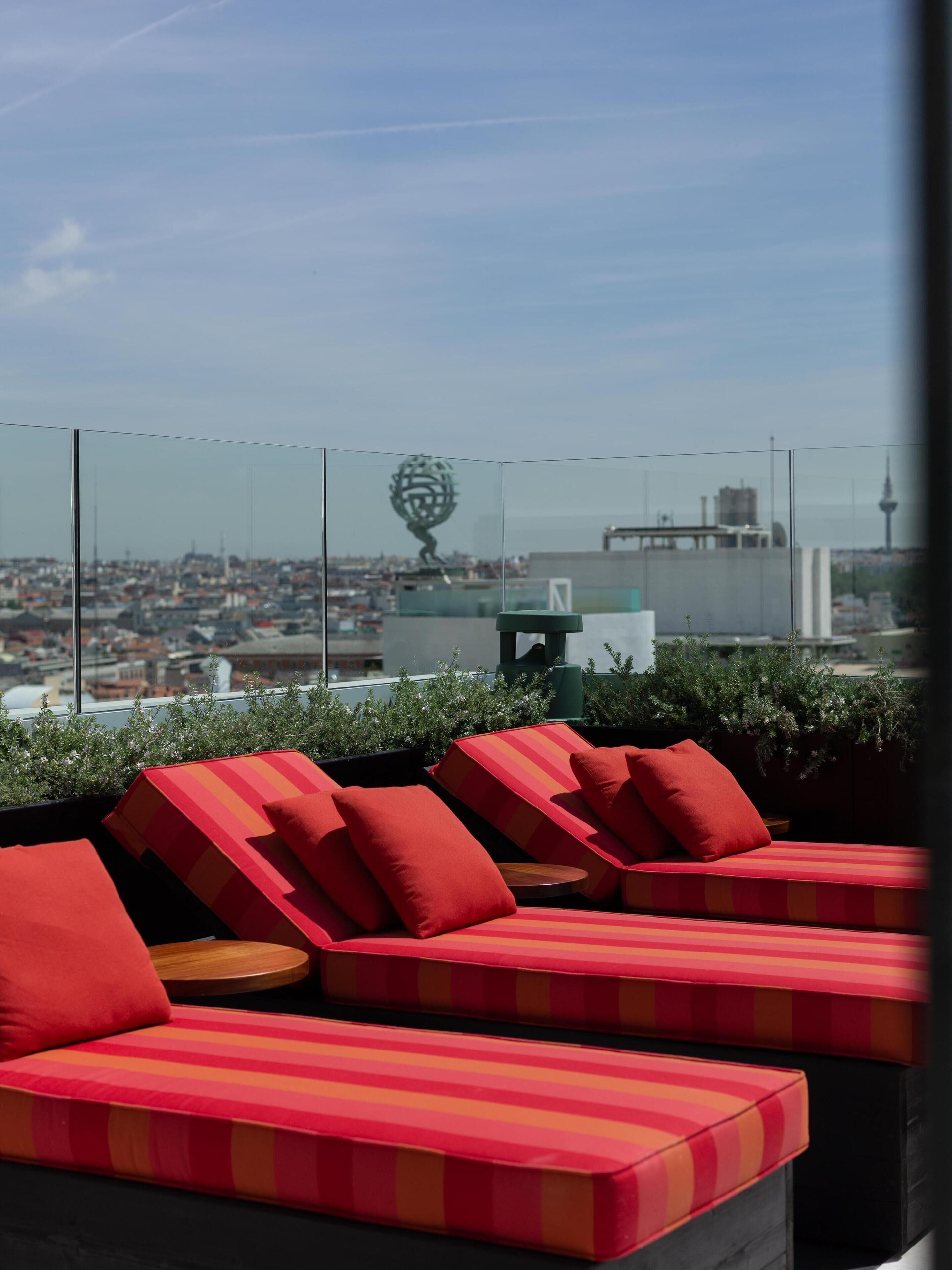 Een dakterras met rood-gestreepte zitplaatsen en uitzicht op een stadsbeeld, inclusief een toren.