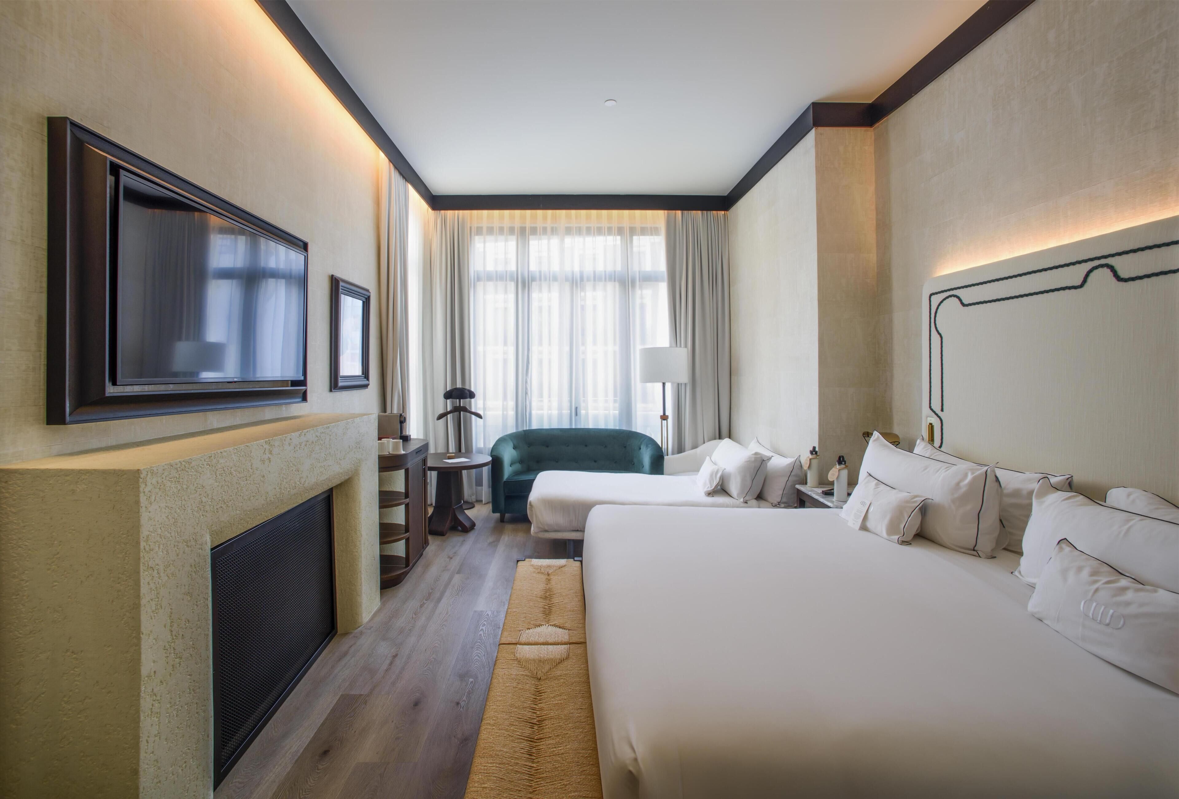 A hotel room with a large bed, a smaller bed, a TV, a fireplace, and a window with curtains.