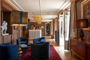 A hotel lobby with a reception desk, blue armchairs, a red carpet, and a chandelier. - Hotel Montera Madrid, Curio Collection By Hilton (Madrid)