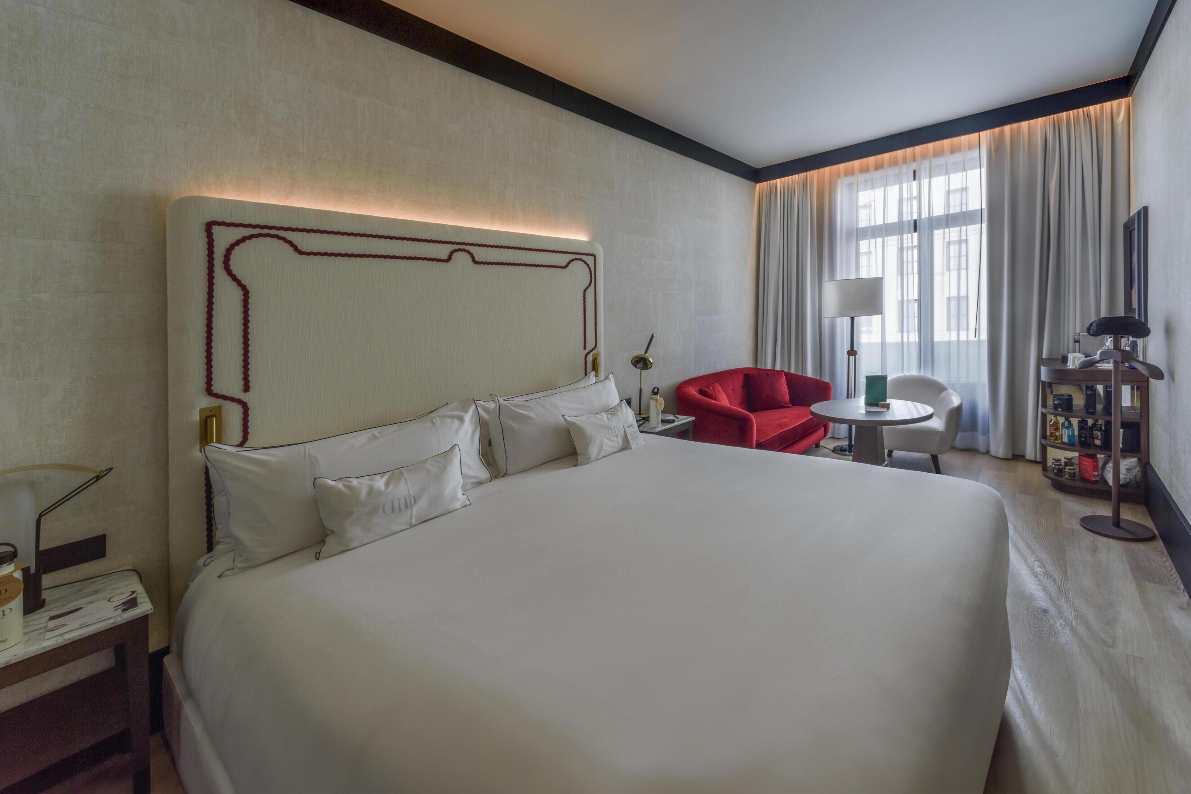 Une chambre d’hôtel avec un grand lit, une chaise rouge, une petite table et une lampe.