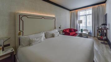 Une chambre d’hôtel avec un grand lit, une chaise rouge, une petite table et une lampe.