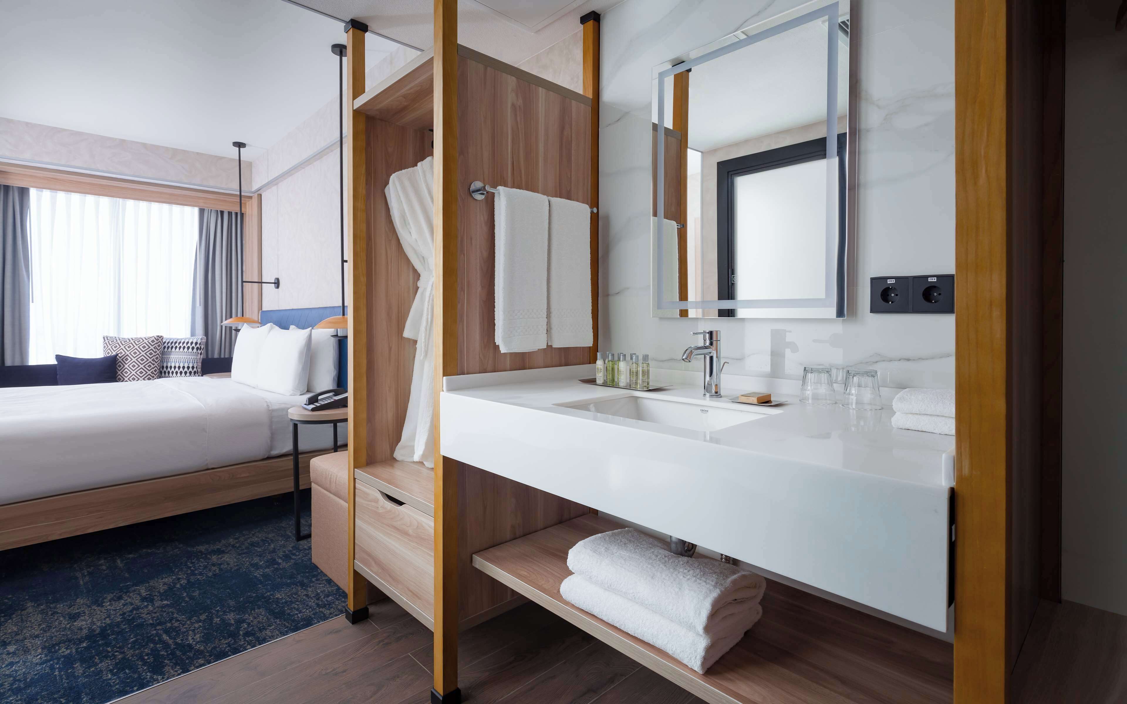A hotel room with a bed, a bathroom with a sink, and a large mirror.