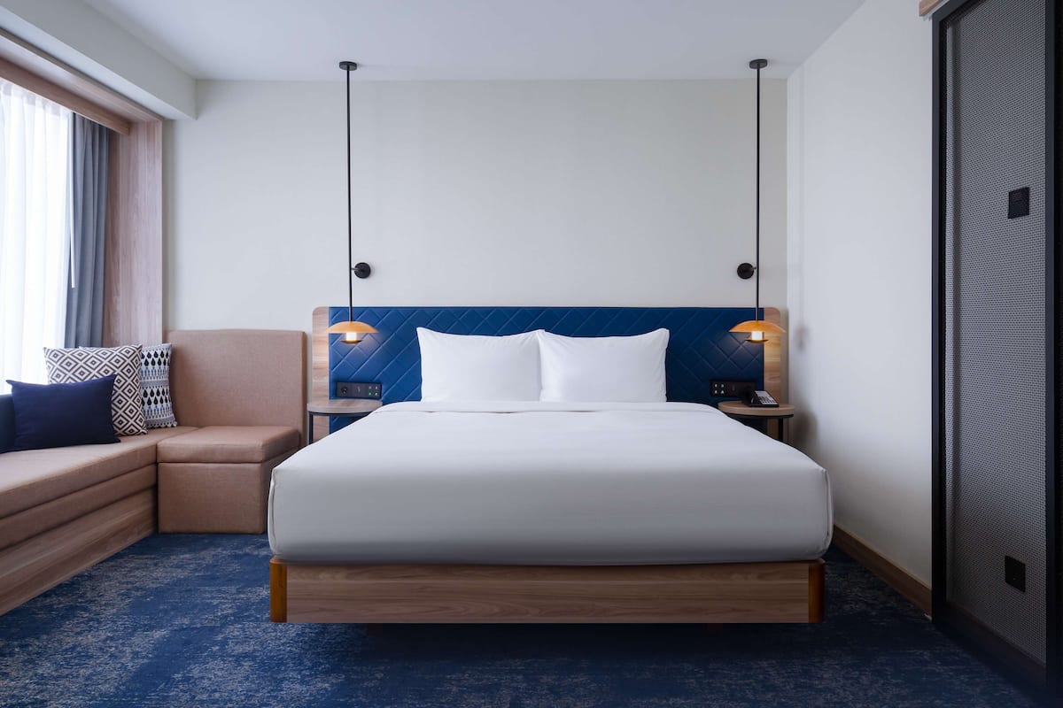 A hotel room with a bed, a sofa, a nightstand, and a large window.