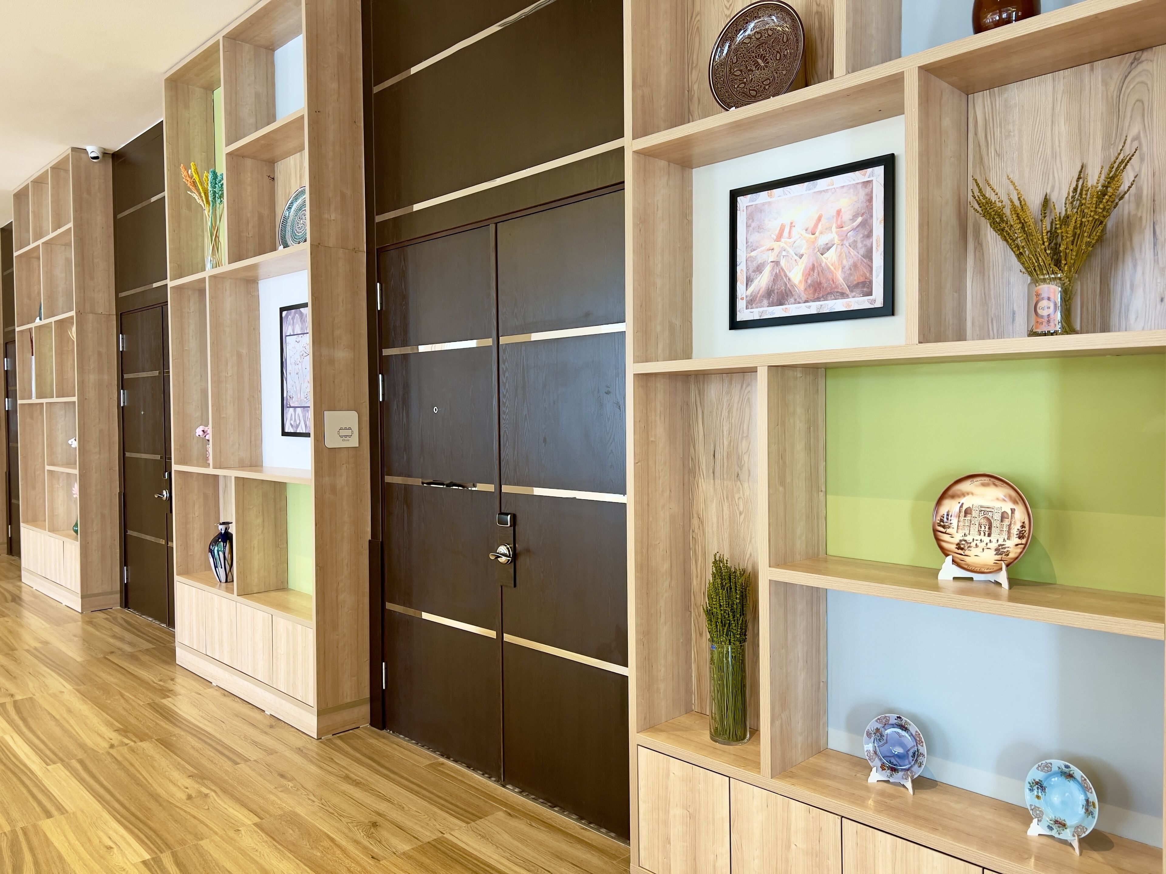Een hotelgang met houten wandplanken waarop diverse decoratieve objecten staan, zoals vazen en kunstwerken in lijsten.