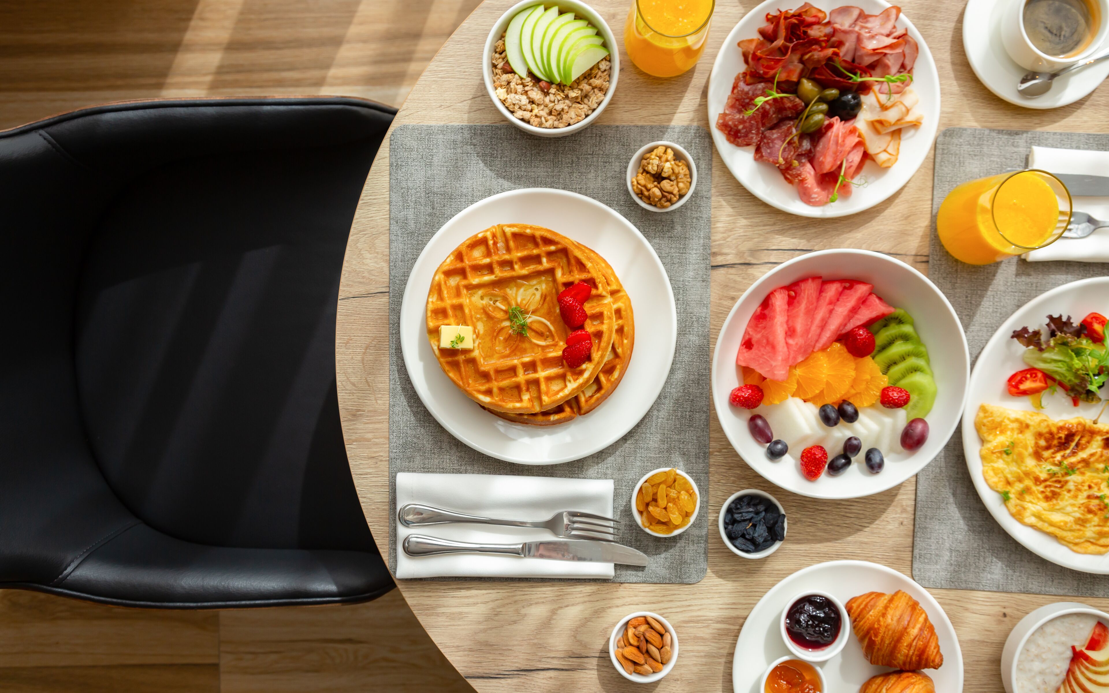 Una colazione con waffle, frutta, pasticcini e una tazza di caffè su un tavolo di legno.