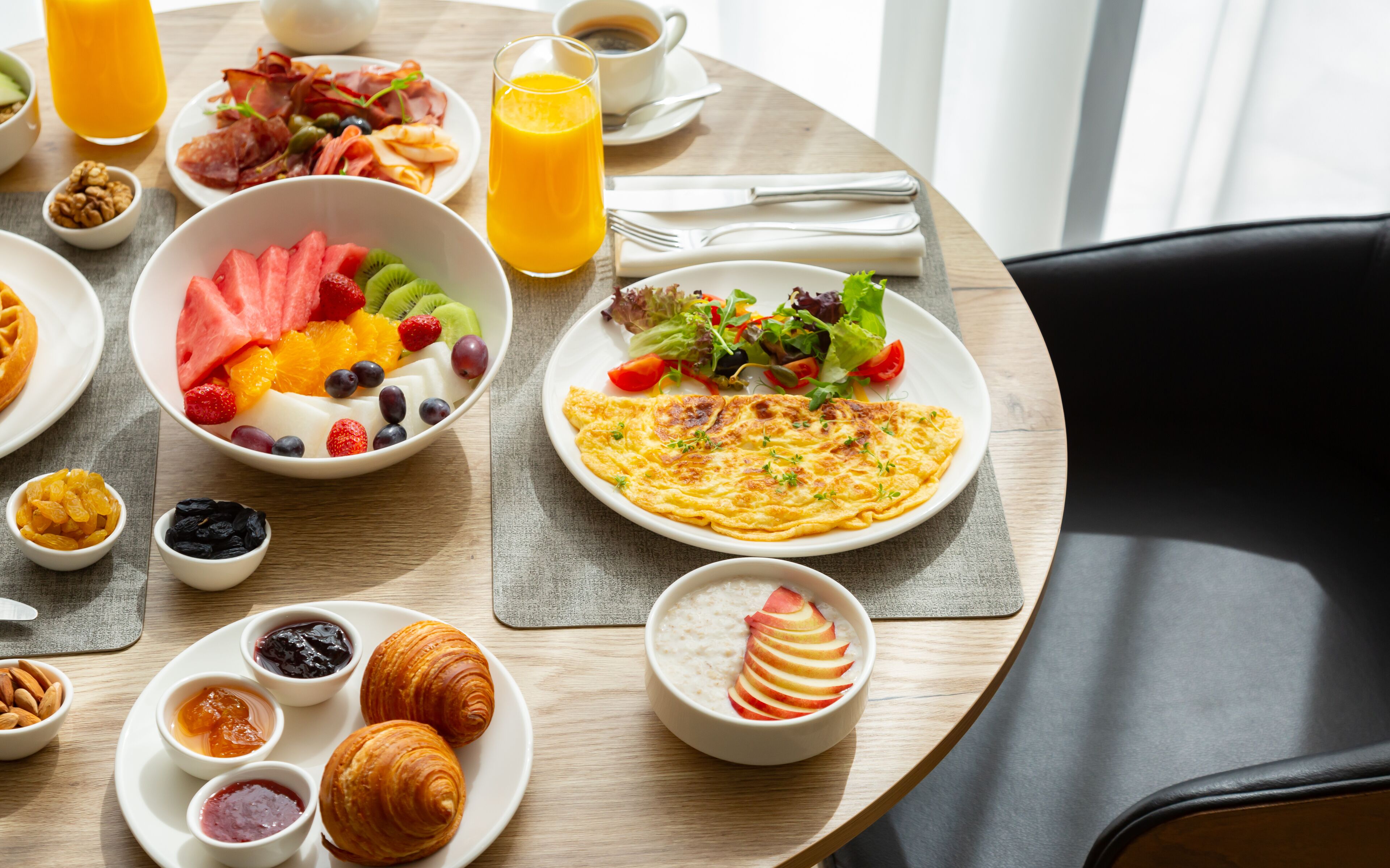 Una mesa de desayuno con diversas opciones de comida, entre ellas frutas, pasteles y un croissant.