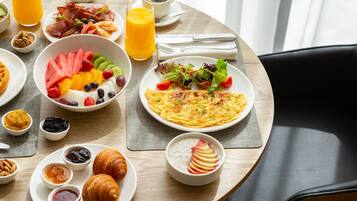 Una mesa de desayuno con diversas opciones de comida, entre ellas frutas, pasteles y un croissant.