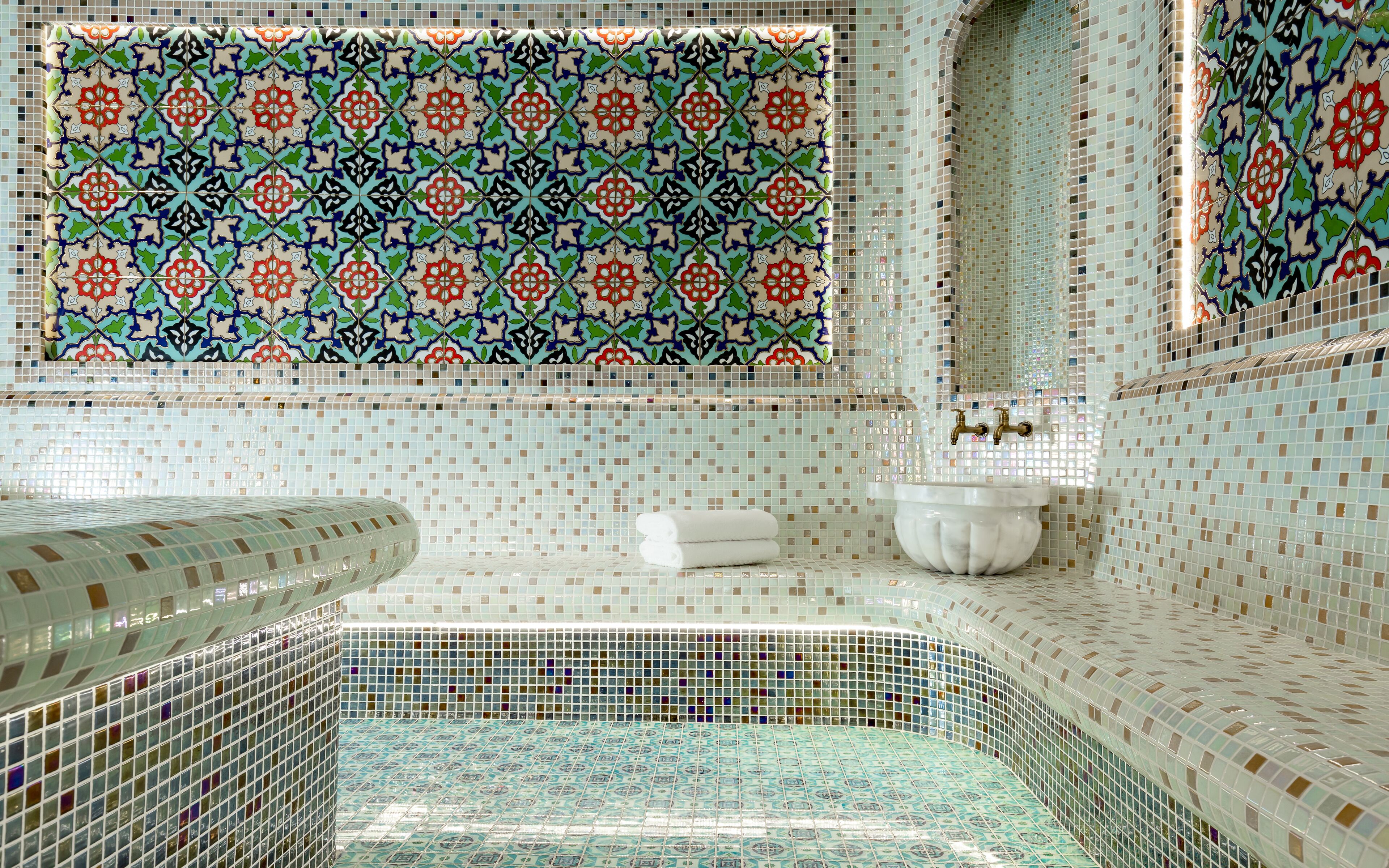 Un baño con pared de mosaicos, un lavamanos blanco y una bañera.