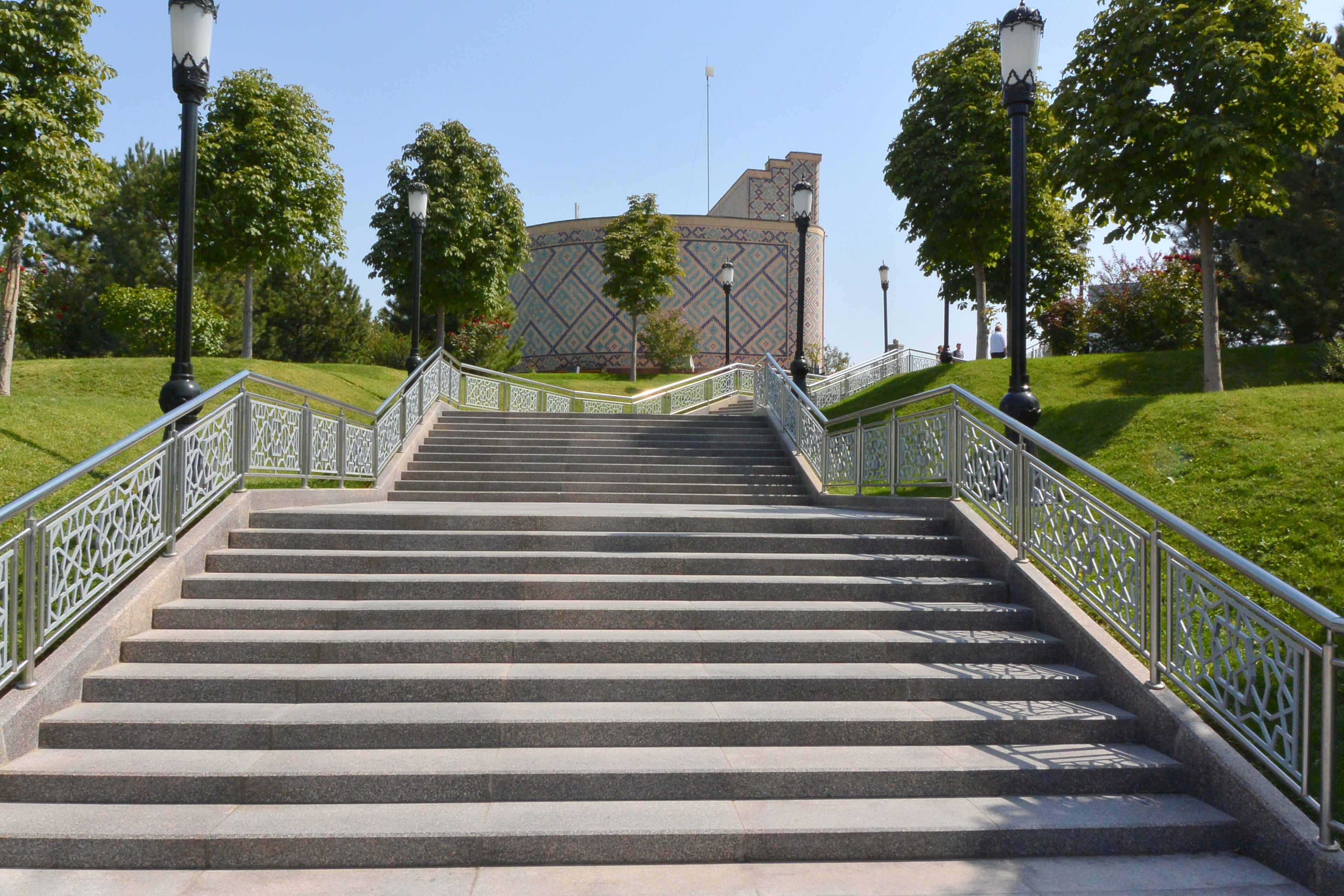 Un conjunto de escalones de piedra que conducen a un edificio con fachada decorativa, rodeado de follaje y barandillas de metal.