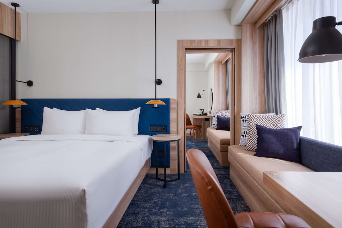 A hotel room with a large bed, a smaller bed, a desk, a chair, and a sofa.