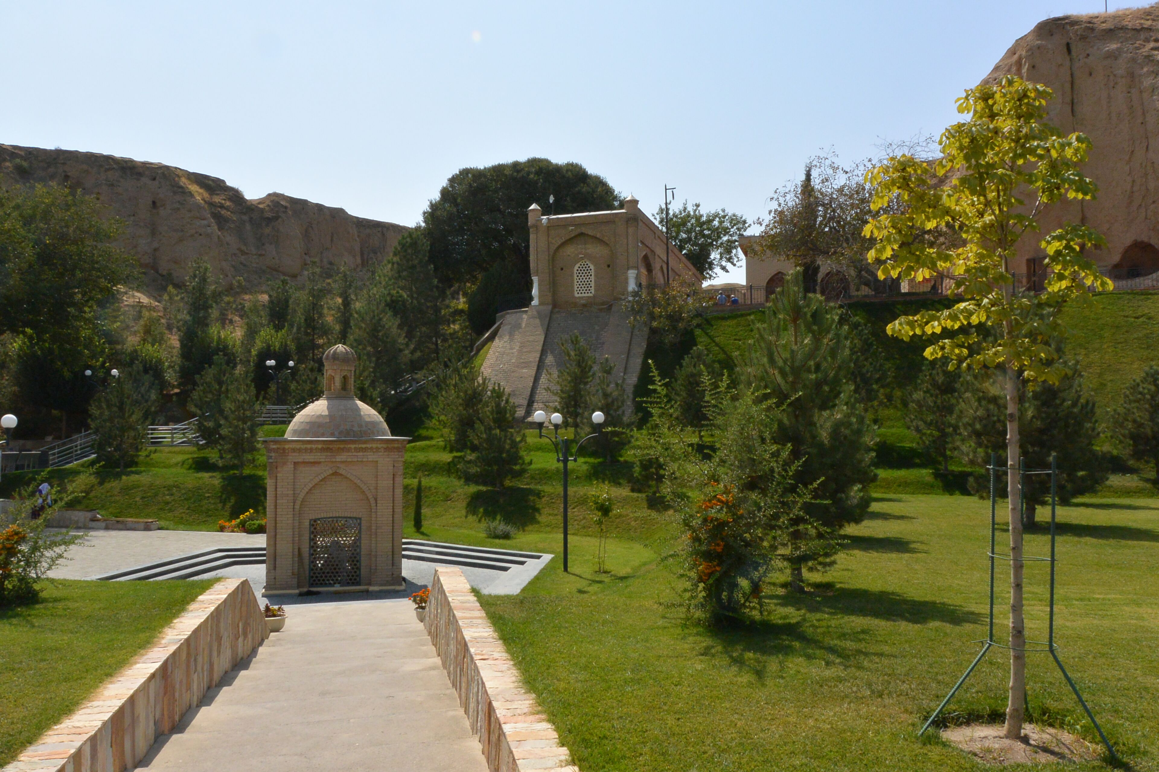 A courtyard with a small building, a staircase, and a large rock formation in the background.