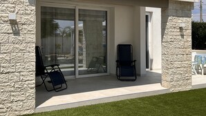 A covered patio with two lounge chairs, a glass door entrance, and a stone exterior. - Villa Samadoel (Santa Maria del Focallo)