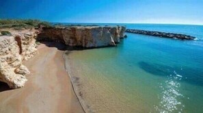 Una playa costera con un acantilado rocoso y aguas tranquilas.