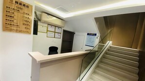 Zona de recepción de un hotel, con mostrador, escalera y una pared con varios avisos.