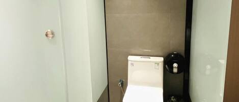 A small, narrow bathroom with a white toilet, a hand dryer, and a trash bin.