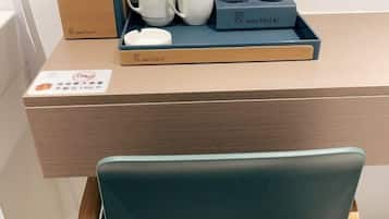 A hotel room with a wooden desk, a tray with white cups and a glass, and a sign indicating a weight limit of 15kg.