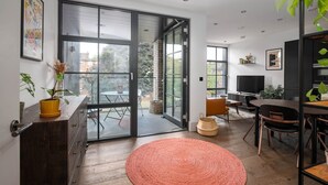 Een moderne woonkamer met een grote schuifpui naar een balkon, een televisie en een eethoek met stoelen.