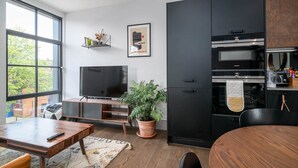 Een moderne keuken met een grote televisie, zwarte kasten en een eethoek met een houten tafel en stoelen.