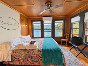 A room with a bed, a chair, a ceiling fan, and large windows overlooking a body of water.