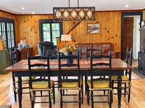 A dining area with a wooden table, black chairs with yellow cushions, a black leather couch, and a hanging light fixture.