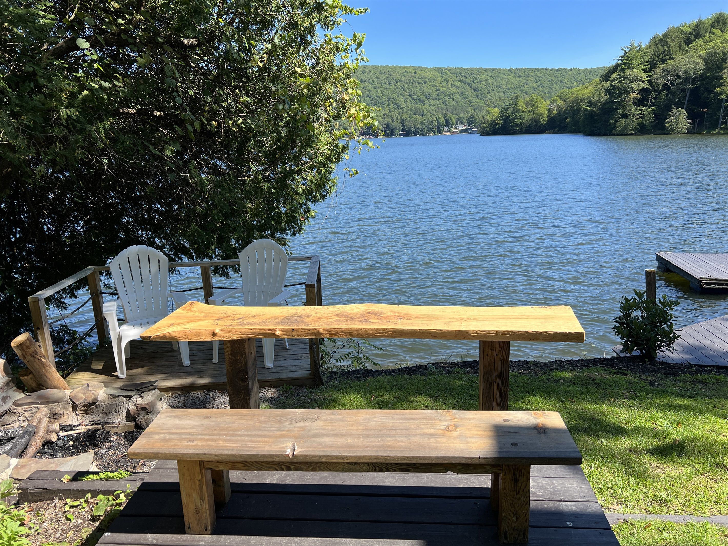 Une table et des chaises en bois, installées près d’un lac, avec un quai et une zone herbeuse.
