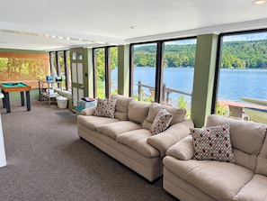 A spacious living area with a large window overlooking a lake, a pool table, and a comfortable sofa set.