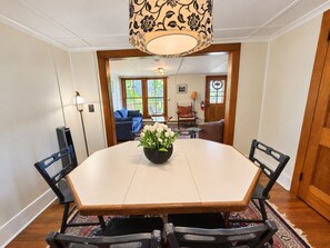 Un comedor con una mesa redonda, sillas, un jarrón de flores y vistas a una sala de estar con un sofá y sillones.
