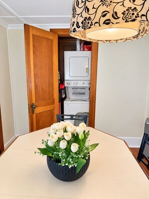 A dining table with a centerpiece of white flowers, a wooden door, and a white appliance in the background.