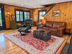 A room with a leather recliner, a brown leather sofa, a vintage suitcase as a coffee table, and a patterned rug.