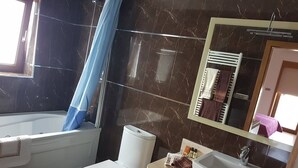 Een badkamer met bad, toilet, wastafel en spiegel met handdoekhouder.