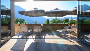 Un patio soleggiato con due ombrelloni, un muro in pietra e vista sulle montagne.