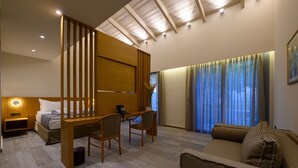 Una camera d'albergo con un letto, una scrivania, due sedie, un divano, un pannello di legno, un comodino, una lampada e una finestra con tende.