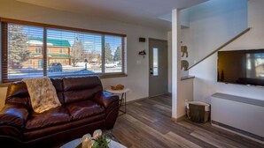 A living room with a leather sofa, a small table, and a TV mounted on the wall. - NEW Condo in Core Area! (Pagosa Springs)