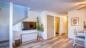 A modern apartment with a staircase, a flat-screen TV, a dining area, and a hallway leading to another room. - NEW Condo in Core Area! (Pagosa Springs)