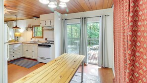 A kitchen with white cabinets, a wooden table, and a view of the outdoors through large windows. - Edgemont Home w/ Deck ~ 9 Mi to Greers Ferry Lake! (Edgemont)