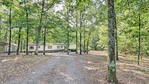 A campsite with a single mobile home, surrounded by dense trees and a gravel path. - Edgemont Home w/ Deck ~ 9 Mi to Greers Ferry Lake! (Edgemont)